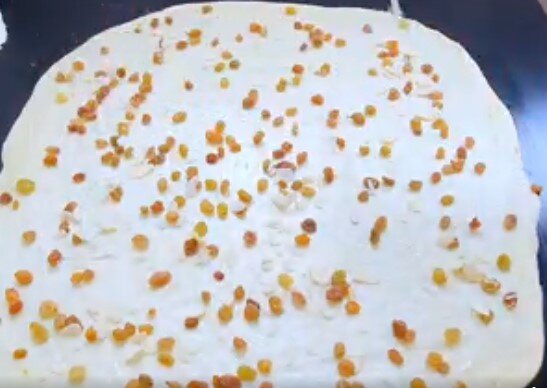 Раскатанное в тонкий пласт и присыпанное изюмом с лепестками миндаля тесто