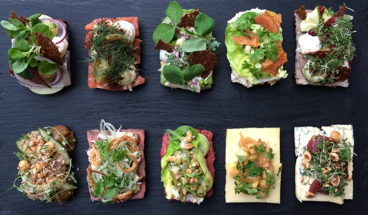 Датская кухня. Смёрреброд. О датской кухне, большинство из нас знает или мало, или совсем ничего. Страна давшая миру Андерсона, Фон Триера и группу Agua, похожа на тихую гавань. Когда, в последний раз, вам доводилось слышать о новостях Дании? Вот и Датская кухня такая же, и даже многолетний триумф ресторана Noma в рейтинге лучших ресторанов мира, в этом смысле мало, что изменил. Впрочем, один факт о кухне Дании, все же можно причислить к известным: смёрреброды. На первый взгляд, вроде бы логично предположить, что обычный бутерброд может быть главным блюдом любой кухни, только в том случае, если больше похвастать совершенно нечем. Но это лишь на первый взгляд, феномен смёрребродов шагнул далеко за пределы своей родины, проникнув и за океан, и в наши просторы. В старые времена смёрреброд выполнял функцию простого, быстрого и недорогого перекуса: датчане мазали ржаной хлеб маслом, клали сверху кусочек сыра, ветчины, или еще чего-то в том же духе, утоляли голод и шли по своим делам. Но в отличие от нашего бутерброда, смёрреброд начал расти в высоту. Популярным смёрреброд стал в 1888 году, когда копенгагенский виноторговец Оскар Давидсен открыл винный бар, при своем магазине, а его жена Петра стала готовить смёрреброды для голодных гостей. О том, как в магазине обстояли дела продажей вина история умалчивает, но слава смёрребродов, которые Петра делала с большой выдумкой, разнеслась по всему Копенгагену. В 1900 году, меню винного бара, в котором на тот момент насчитывалось уже 178 вариаций смёрребродов, попала в книгу рекордов Гиннеса, как самое длинное меню в мире, боллее 140 см! И датские бутерброды вышли на мировую арену. Сегодня смёрреброд, визитная карточка Датской кухни. Ниже приготовим 3 вида смёрребродов, поехали!