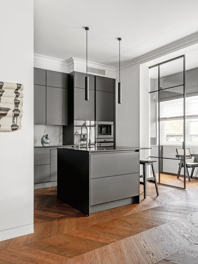 Выбор кухни пал на фабрику SieMatic. Она встроена в небольшую нишу, а мойка вынесена на небольшой остров. Хозяева квартиры не побоялись концептуального чёрного цвета фасадов. На стене — декоративное керамическое панно, Savour.