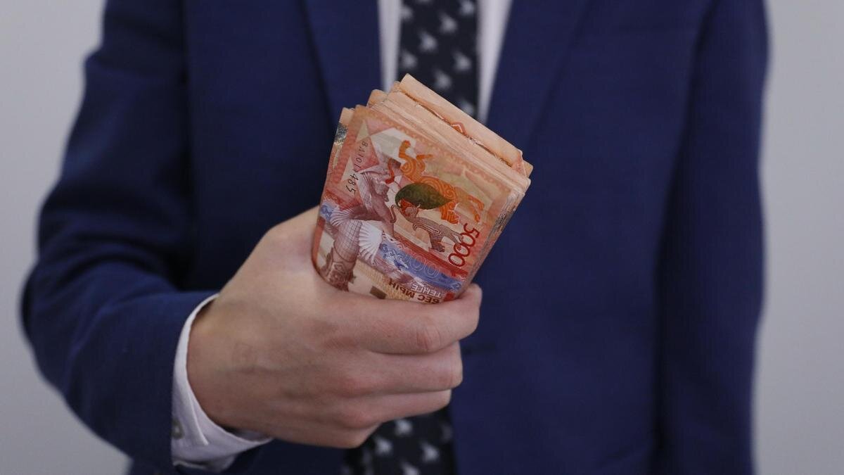   Мужчина в костюме держит пачку денег:NUR.KZ / Петр Карандашов