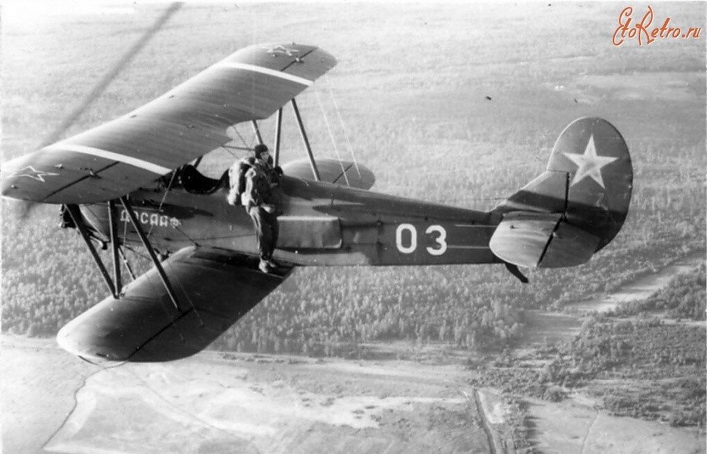 На этой фотографии видно, что парашютист (взрослый) вылез из передней кабины на левое нижнее крыло. Он стоит на специальной твёрдой площадке и готовится к прыжку.