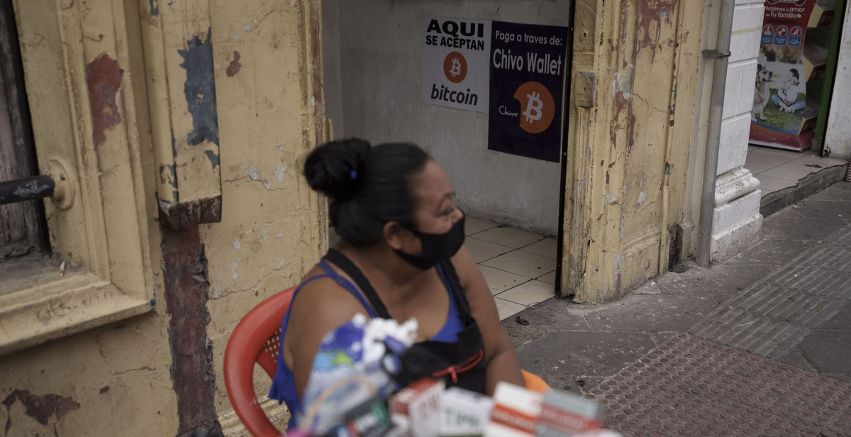 Уличная продавщица сидит возле магазина сотовых телефонов с надписью "Мы принимаем биткоин" на двери, в Сан-Сальвадоре, Сальвадор. МОЙЗЕС КАСТИЛЬО/ASSOCIATED PRESS