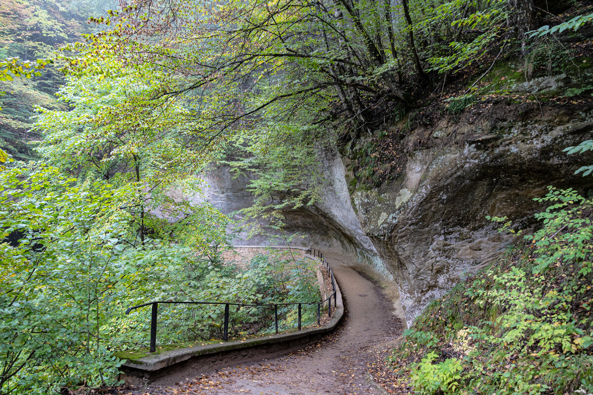1. Незадолго до подножия горы Красное Солнышко пешеходная дорожка проходит под полукруглым скальным навесом. С противоположной стороны пути установлены перила.