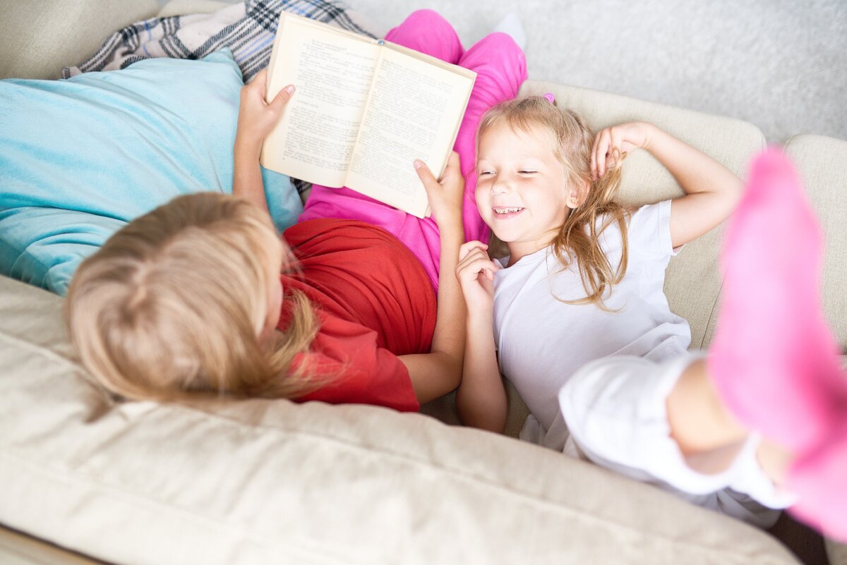 Спящую сестру читать. Чтение на диване дети. Ребёнок лежит на сестре. Маленькая девочка книгу читает на диване. Картинки дети читают на диване.