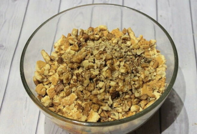 Грецкие орехи дробим и выкладываем в емкость с измельченным печеньем. 