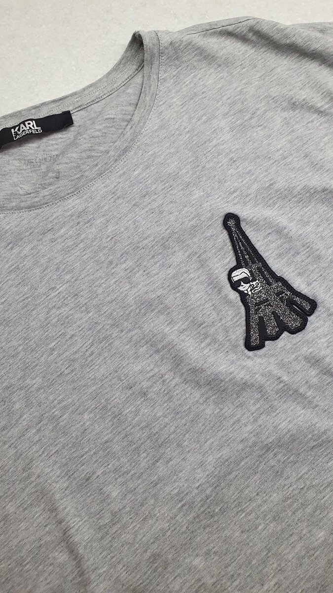 На спине написано название бренда, а на груди аппликация в виде Эйфелевой башни и Карла Лагерфельда, выглядывающего из неё со своей любимицей- кошкой Шуппет. 