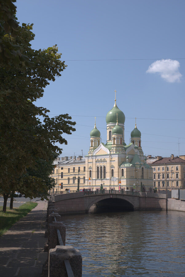 Съёмка в солнечную погоду приводит к избыточной контрастности: цвета зданий получились слишком светлыми и выглядят блёкло и невыразительно, тени слишком глубокие, а листва на деревьях слева тёмная и фактура её почти неразличима. Глобальный контраст слишком велик, а локальный – недостаточен. Обычно в таких ситуациях больше всего страдает небо, но это фото было намеренно проэкспонировано с недодержкой, чтобы сохранить фактуру на облачке. При нормальной экспозиции "по среднему" фактура и облака, и белых деталей церкви была бы безвозвратно потеряна.