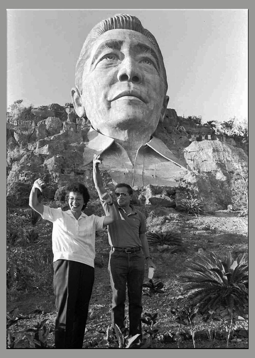 Филиппинские оппозиционеры позируют на фоне бюста Маркоса, показывая палец вниз