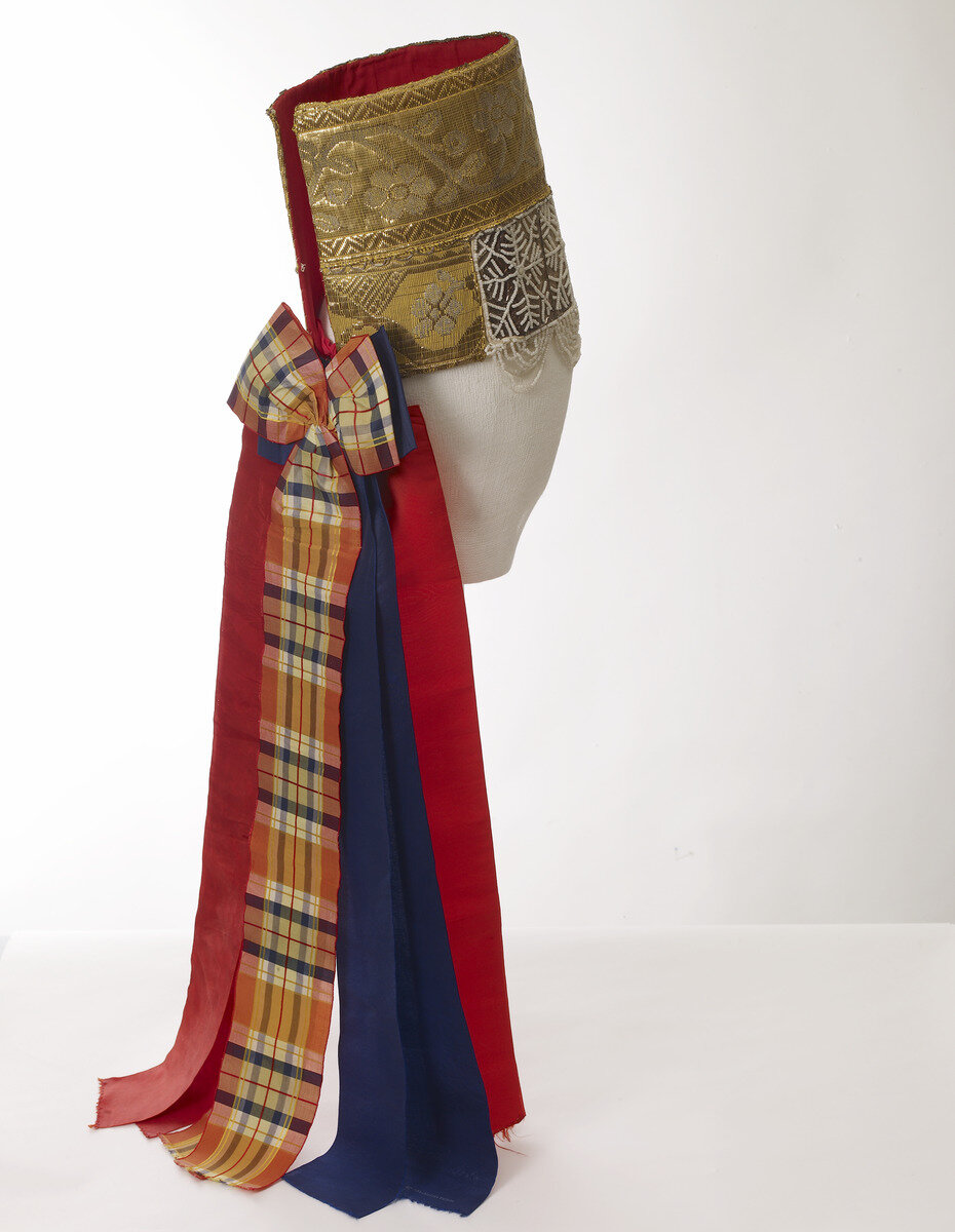 Повязка - высокий праздничный головной убор в форме цилиндра.
Описание предмета. (Перевод с финского языка):

"Повязка" девичья: твердая бумага с пришитой красной подкладкой и переплетом с золотой  лентой вверху и серебряной бумагой (ред. обычно фольга) с жемчугом внизу; разноцветные шелковые ленты свисают со спины.

Головной убор девушки высокий, укреплен фольгой или картоном. Головной убор обтянут серебристой бумагой, на которую нашито сетчатое украшение из мелких стеклянных бусин. С нижнего края головного убора изогнуто свисают нити из таких же бусин. К верхней части головного убора пришита широкая лента из золотых нитей с цветочно-лиственным мотивом. Головной убор затягивается на голове двумя тканевыми лентами синего цвета. На шее можно завязать большой бант, который завязывается из широкой красной шелковой ленты.

Украшение: жемчужное украшение

Национальный музей Финляндии

Измерения
высота: 24,0 см
диаметр: 18,0 см
длина, самая большая, декоративные полосы: 63,0 см

Время изготовления до 1911 года
Техника: ручная работа
Техника: рукоделие_текстиль/шитье
Техника: ручная работа_текстиль/нарезание резьбы
декоративные ленты: Техника: рукоделие_текстиль/шитье
Материал: ткань/парча
Материал: ткань/шелк
Материал: жемчуг/стекло
Материал: декоративные ленты: ткань/шелк
основной материал: картон
Россия, Архангельск, Петрогорская

Праздничный головной убор для девушки. Волосы заплетены в одну косу, а на голове повязана красная шелковая лента.
