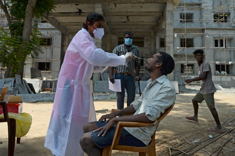Медицинский работник берет образец у человека для теста на COVID на строительной площадке в Ченнаи