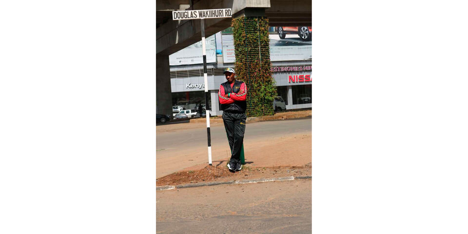 Легенда марафона Кении Дуглас Вакиихури позирует рядом со знаком дороги.