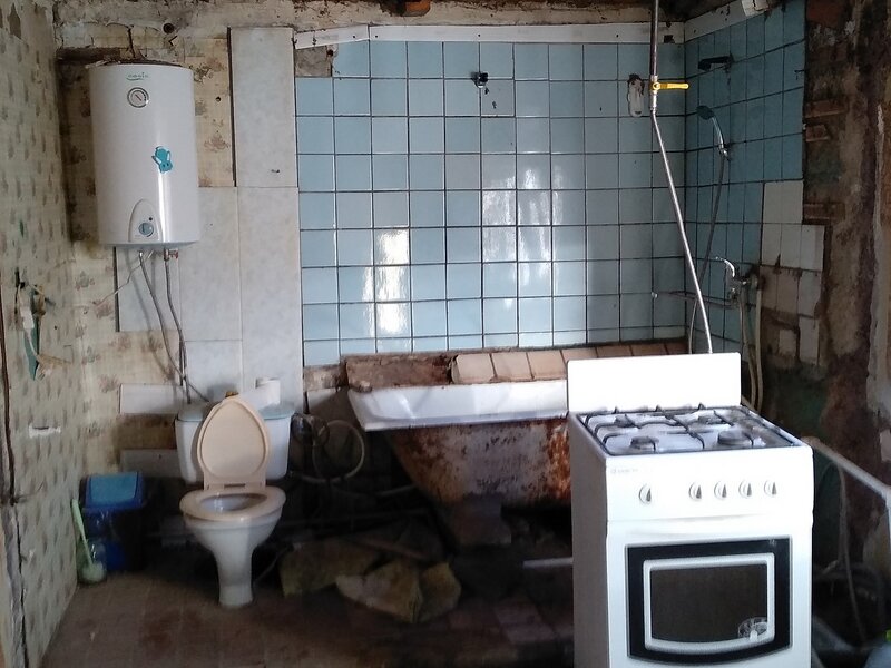 Вид совмещённого санузла в доме до ремонта со старой ванной, устаревшей плиткой