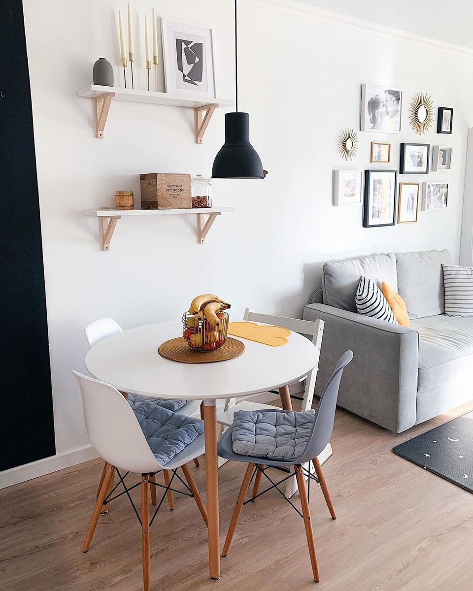 Столовую группу расположили сразу за грифельной акцентной стеной. Она разделяет две функциональные зоны и контрастирует как с белыми фасадами шкафов, так и с обеденным столом.