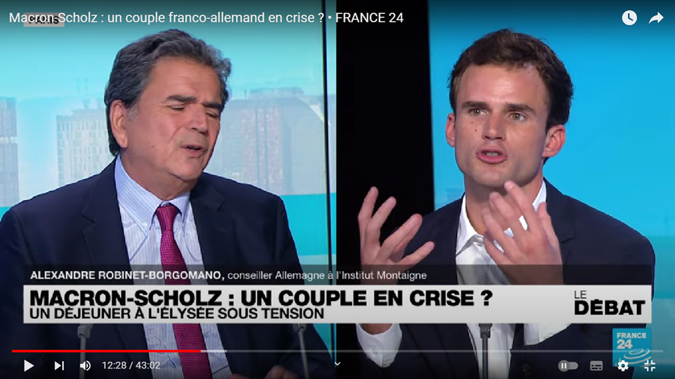 Пух и перья в студии. Реакция Леллюша (слева) на слова немецкого советника Александра Робине-Боргомана о его  антинемецких настроениях.