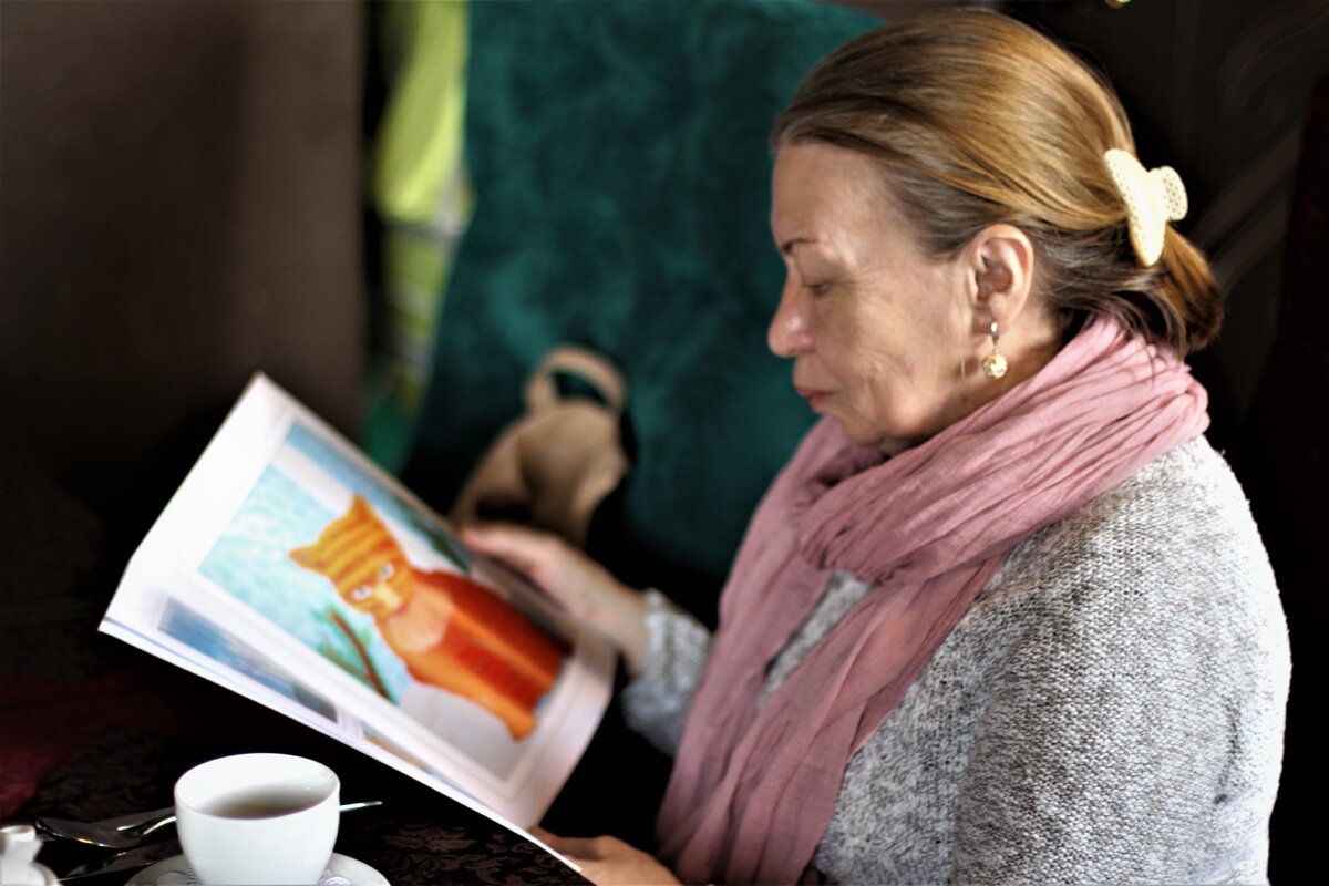 Подпись: Ольга Разумовская листает альбом с рисунками своих учеников