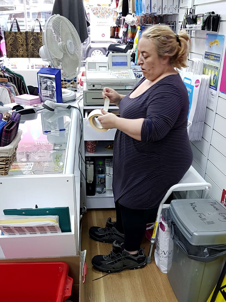 Начальница магазина за прилавком. Ради хохмы она одела ботинки большого размера, принесенные как пожертвование на продажу. Фотография из личного архива