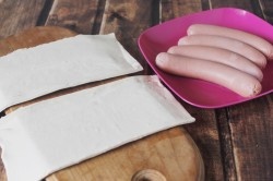 ШАГ 1:
Возьмем из упаковки слоеного теста два пласта (обычно в пачке их четыре, два остальных спрячем назад в морозилку). Подождем, пока они немного разморозятся. Сварим сосиски до полуготовности - 2 минуты будет достаточно. Дадим им остыть и высохнуть - можно дополнительно промакнуть их бумажным полотенцем. Можно предварительно сосиски не варить, но мне так больше нравится.