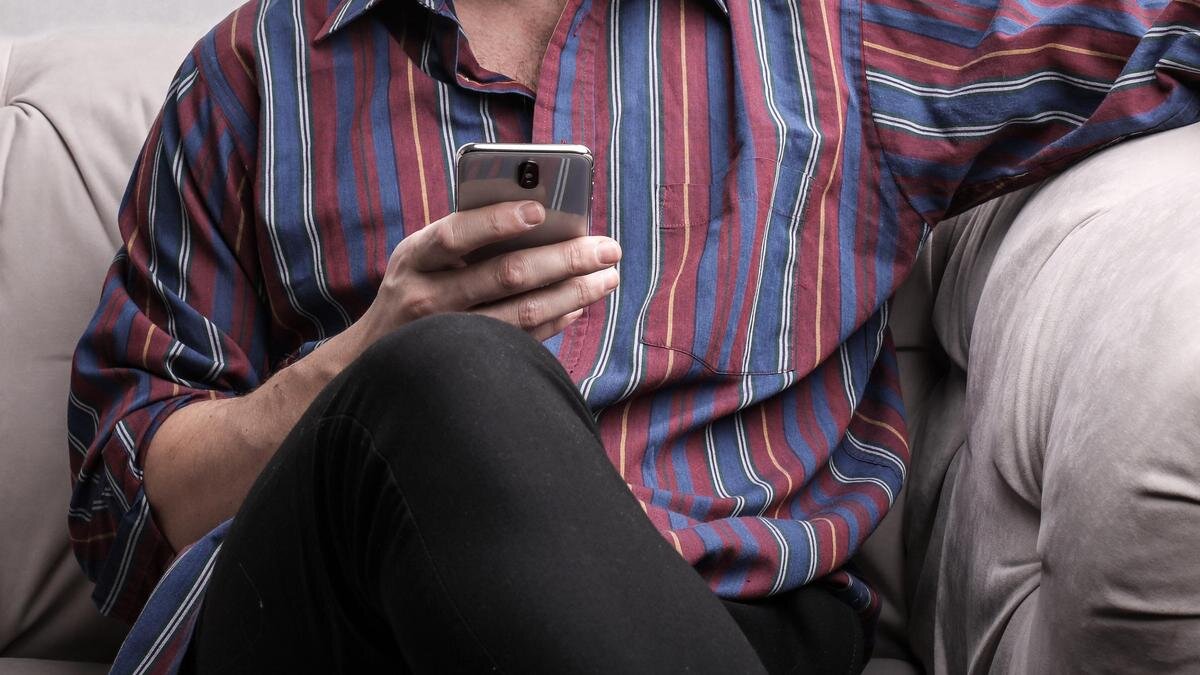    Мужчина сидит на диване с телефоном в руках:pexels.com