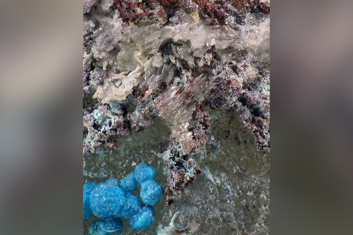 На фото: белые волосовидные кристаллы сергейсмирновита с голубым епифановитом и темно-красными агрегатами самородной меди