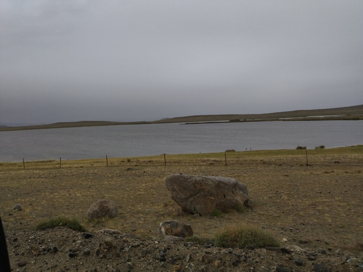 Забор с колючей проволокой между дорогой и озером.