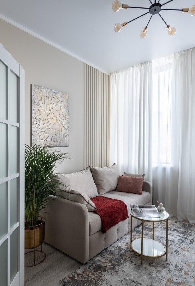 Окраску стен в комнате выполнили в тёплом бежевом оттенке. Разнообразить нейтральную цветовую гамму помогают рельефные панели и фактурные картины. Диван практически сливается с фоном, из-за чего его габариты кажутся меньше.