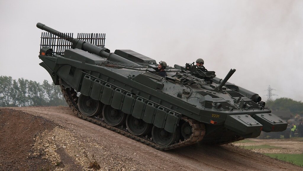 Strv. 103 модификации "C" на полигоне. Обращает на себя внимание целая батарея из топливных канистр, закреплённых с левого борта танка - это импровизированная противокумулятивная защита экипажа в наиболее уязвимом для поражения месте
