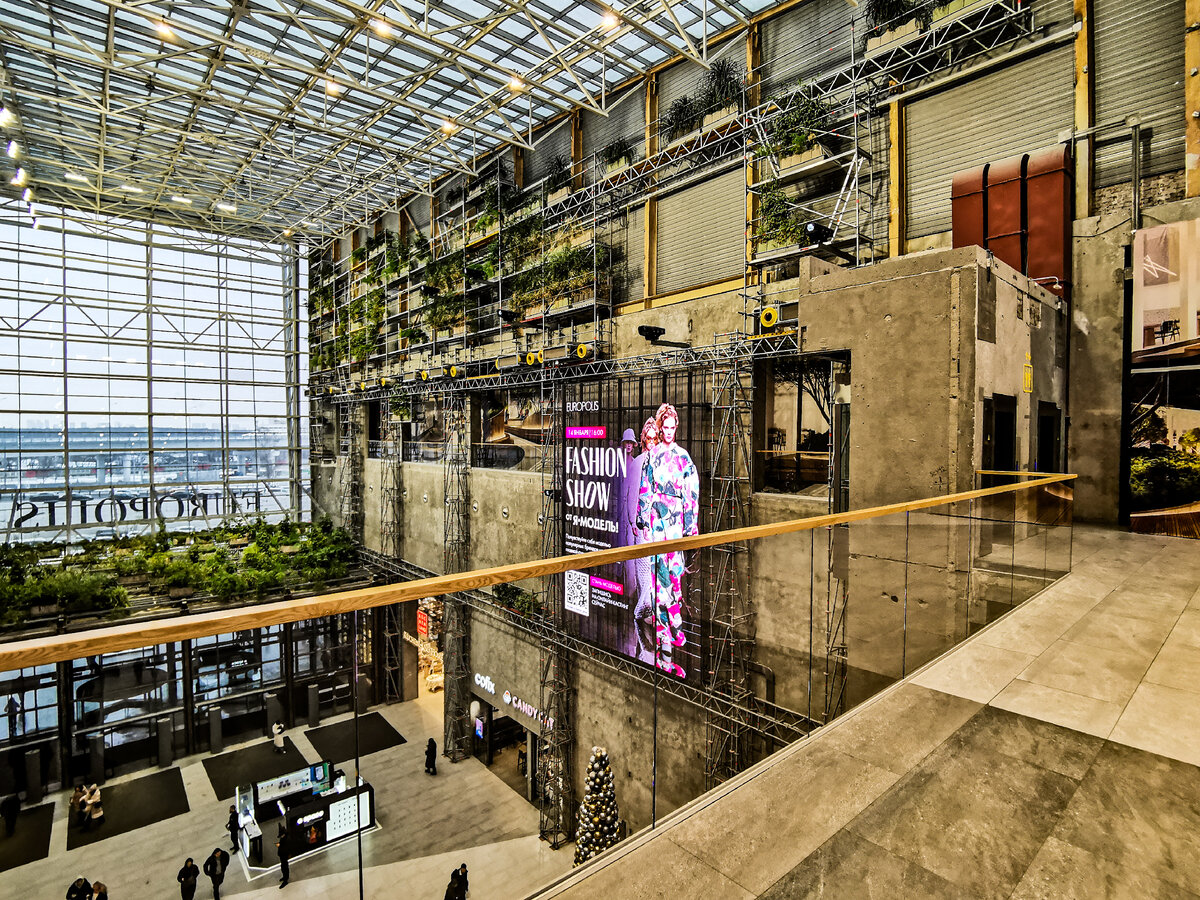 Вид на вход в торговый центр со второго этажа. Справа должен был располагаться ресторан, основной фишкой которого должны были бы зелёные растения и панорамный вид на проспект Мира. Но он, похоже, так и не открылся. А стена выглядит очень необычно.