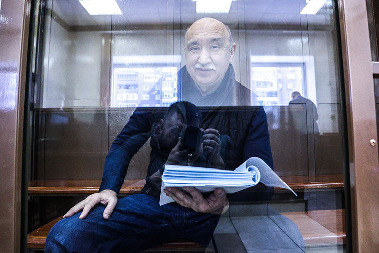    Когда слушатели зашли в зал, Гафуров уже дожидался заседания в «аквариуме». Одетый в темно-синюю кофту, черную жилетку и джинсы, он изучал весомую стопку документов