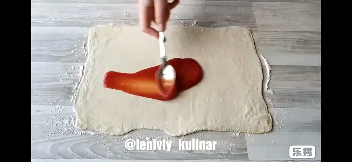 Раскатываем пласт слоеного теста (250 г) и смазываем его кетчупом или томатным соусом