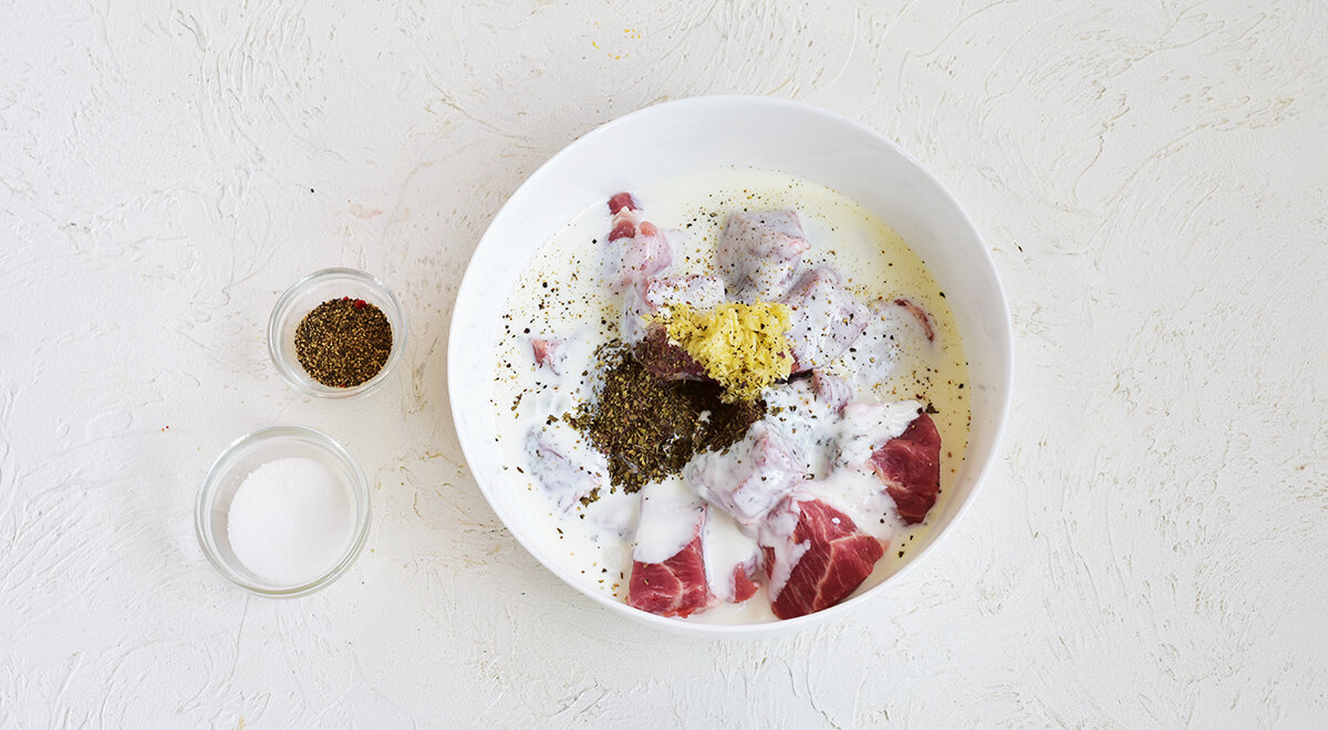 1. Подготовьте свинину. Вымойте и нарежьте крупными кубиками. Для маринада чеснок очистите и пропустите через пресс в большую миску. Влейте кефир, добавьте сушеные прованские травы. Посолите и поперчите по вкусу, переложите свинину в маринад.