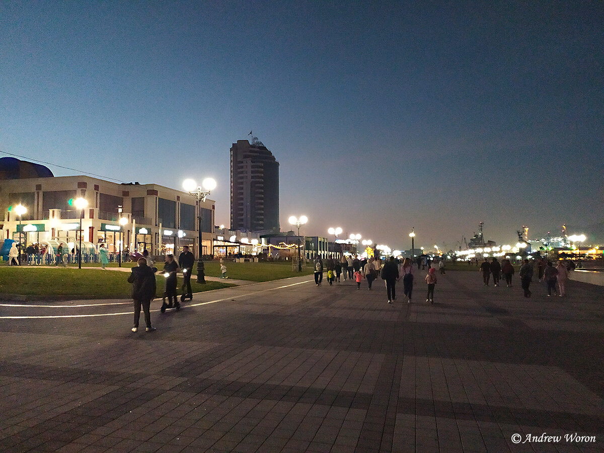 Набережная адмирала Серебрякова в районе Морского вокзала. Людей гуляет очень много, работают кафе и кофейни, большая детская площадка. Молодежь катается на велосипедах и самокатах, и даже саксофонист играет у памятника основателям города