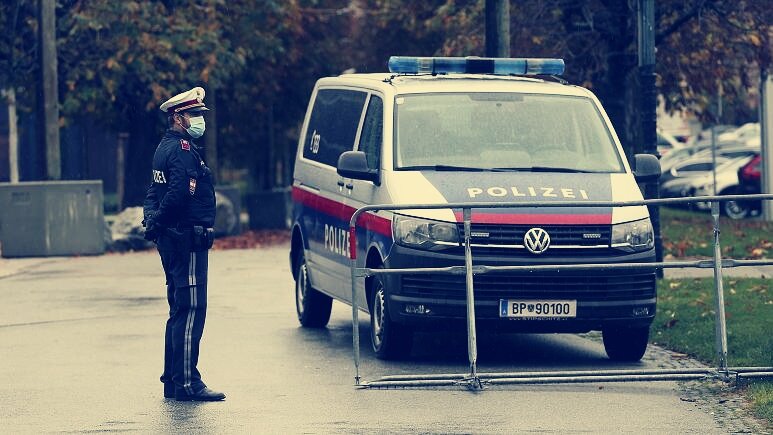 Полицейский в маске стоит за шлагбаумом в центре Вены. 