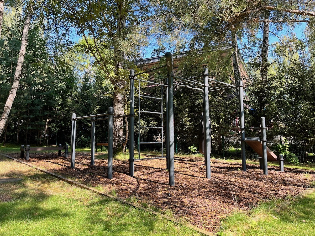 Площадка для воркаута во дворе загородного дома: столбы и перекладины — чёрный муар, хомуты — чёрный муар, покрытие — кора