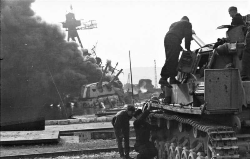 Экипаж танка Pz.Kpfw. IV 7-й дивизии 25-го танкового полка 7-й танковой дивизии вермахта у горящего французского тяжелого крейсера «Кольбер».  Крейсер был затоплен подрывом, несмотря на присутствие немецких офицеров на борту. Впоследствии на нем детонировали артиллерийские погреба, вследствие чего корабль был полностью разрушен.