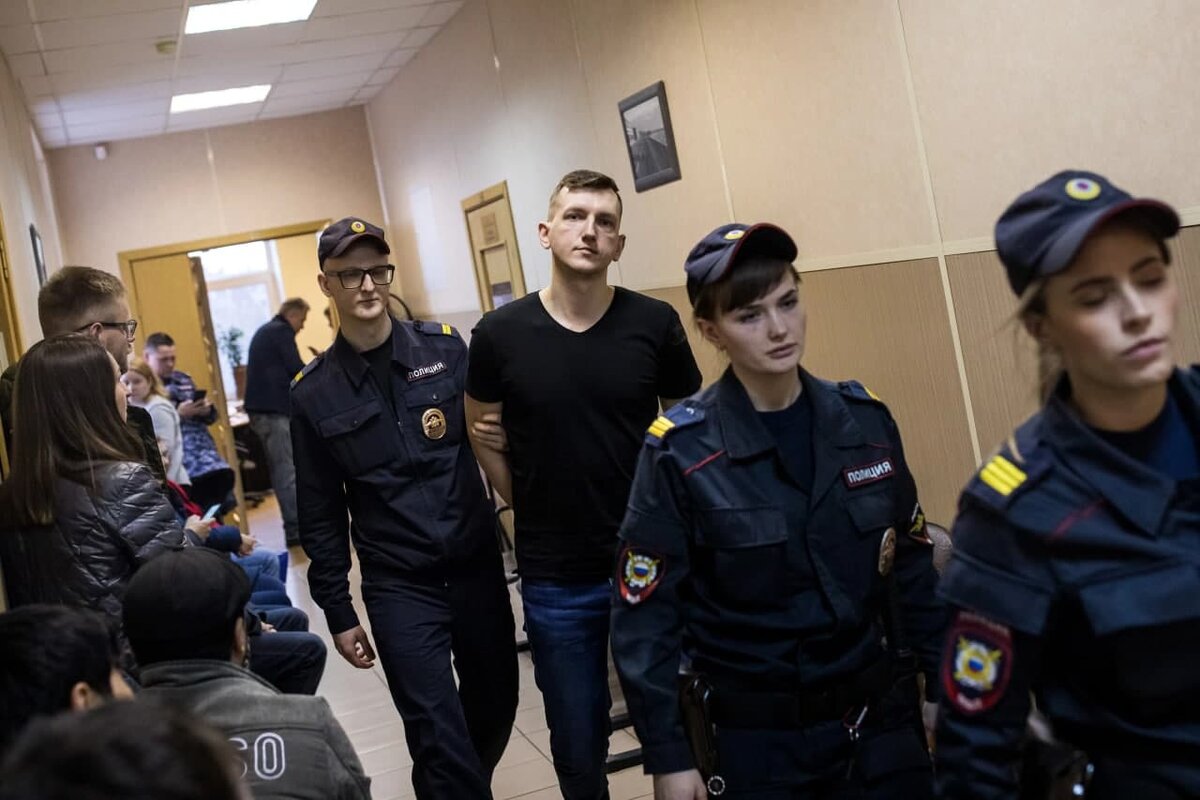 Экс-силовика из Санкт-Петербурга (на фото под конвоем) обвиняют в превышении должностных полномочий, хранении наркотиков и получении взяток в крупном размере. Фото от тлг-канала "360". 