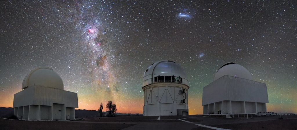    The stars and dust lanes of the Milky Way hang above telescope domes in this richly hued image of Cerro Tololo Inter-American Observatory (CTIO), a program of NSF’s NOIRLab. The two bright, wispy ovals to the right are the Large and Small Magellanic Clouds, dwarf galaxies visible only in the southern hemisphere. The band of color along the horizon is a phenomenon known as airglow, a visible reaction between molecules in Earth’s atmosphere and solar radiation. In this picture are the Curtis Schmidt Telescope (left), the Víctor M. Blanco 4-meter Telescope (middle), and the SMARTS 1.5-meter Telescope (right). These telescopes, alongside 12 others, comprise CTIO, the principal ground-based optical platform for US astronomical investigation of the southern skies. Александр Шереметьев