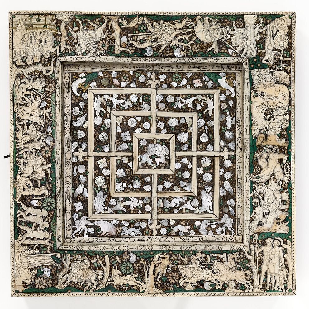 Доска для игры в мельницу.  Не будем разъяснять здесь правила игры, а лучше полюбуемся красотой этого гармоничного произведения. В центре находится квадратное игровое поле. Более яркие белые фигуры людей и животных — перламутр, а полоски поля и орнаменты на широкой наружной рамке — инкрустация из кости. Зеленые детали это тоже слоновая кость, окрашенная травяным красителем. 