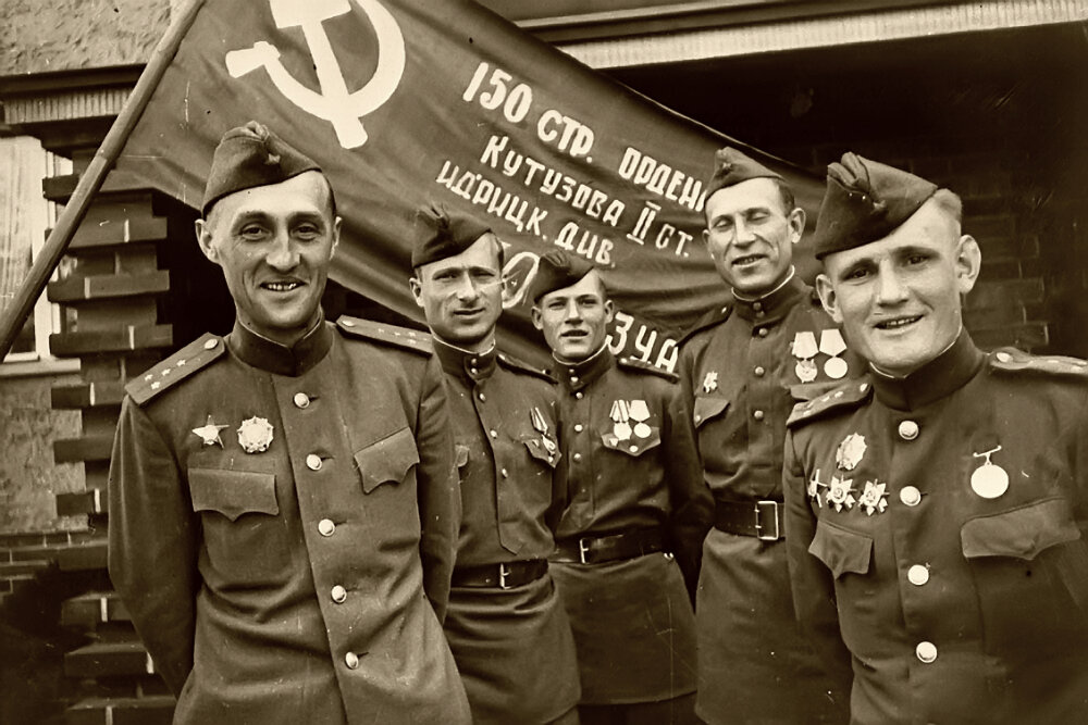 Военнослужащие 150-й Идрицкой стрелковой дивизии на фоне своего штурмового флага, водруженного 01 мая 1945 года над зданием рейхстага в Берлине и ставшего впоследствии государственной реликвией России — Знаменем Победы. На фото участники штурма Рейхстага, провожавшие флаг в Москву с берлинского аэродрома Темпельгоф 20 июня 1945 года (слева направо): капитан К.Я. Самсонов, младший сержант М.В. Кантария, сержант М.А. Егоров, старший сержант Илья Яковлевич Сьянов (1905—1988), капитан С.А. Неустроев. 20.06.1945 г.