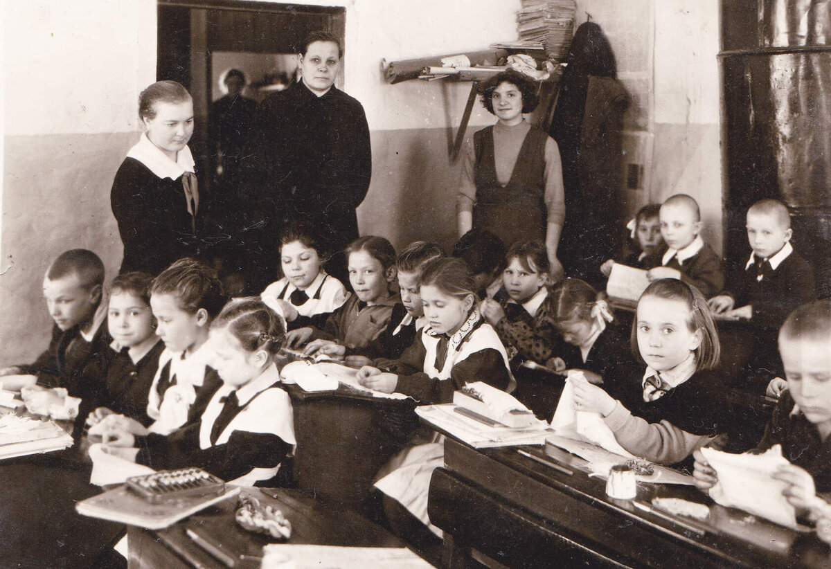 В дверях стоит Евгения Павловна. Танюша сидит вторая справа, смотрит в камеру.