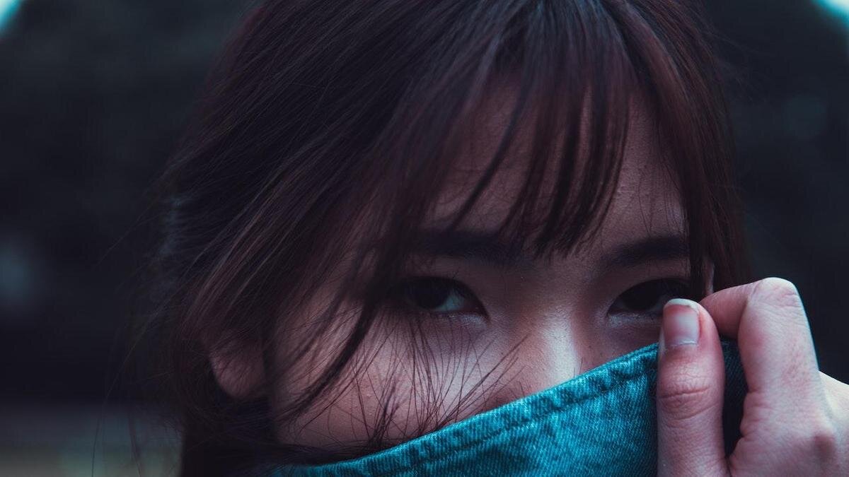    Девушка азиатской внешнгости с челкой прикрывает лицо воротом джинсовой куртки:Pexels