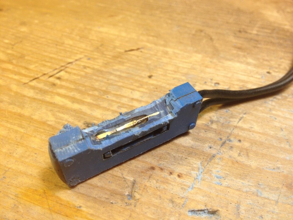 Разрезанная ровно вдоль колба старого геркона. Видны 2 контакта, замыкаемых магнитом.