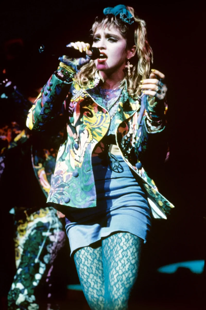 Выступление на сцене в мини-юбке, жакете с принтом, бирюзовых кружевных колготках и головном платке.