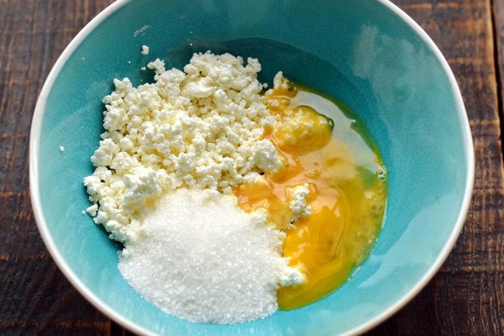 1. В первую очередь приготовьте творожную начинку. Творог поместите в глубокую емкость, всыпьте сахарный песок, вбейте одно яйцо.