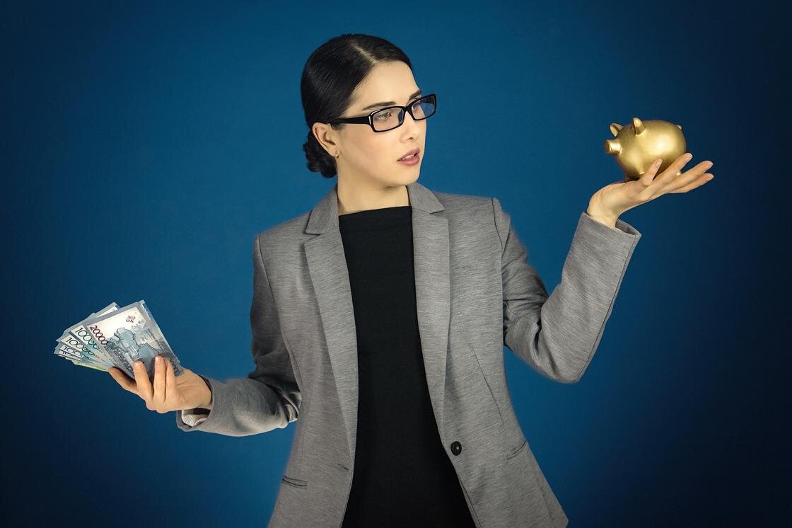    Женщина с деньгами в руках смотрит на копилку:Roman Chekhovskoy/Getty Images