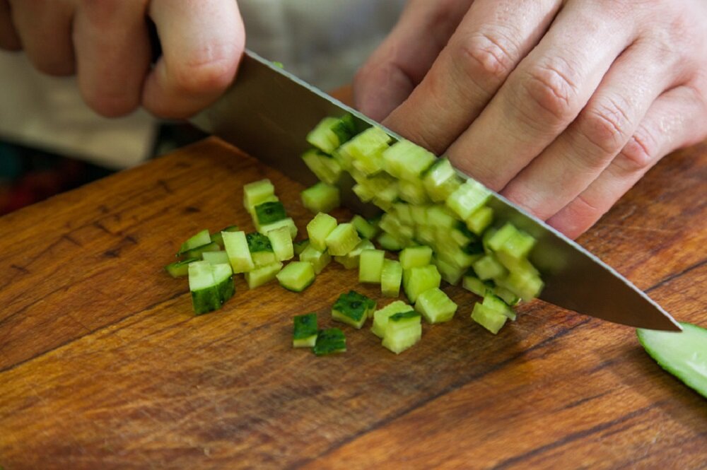 Нож режет овощи. Огурцы порезанные кубиками. Мелко нарезанный огурец. Мелко нарезанные овощи. Свежие огурцы кубиками.