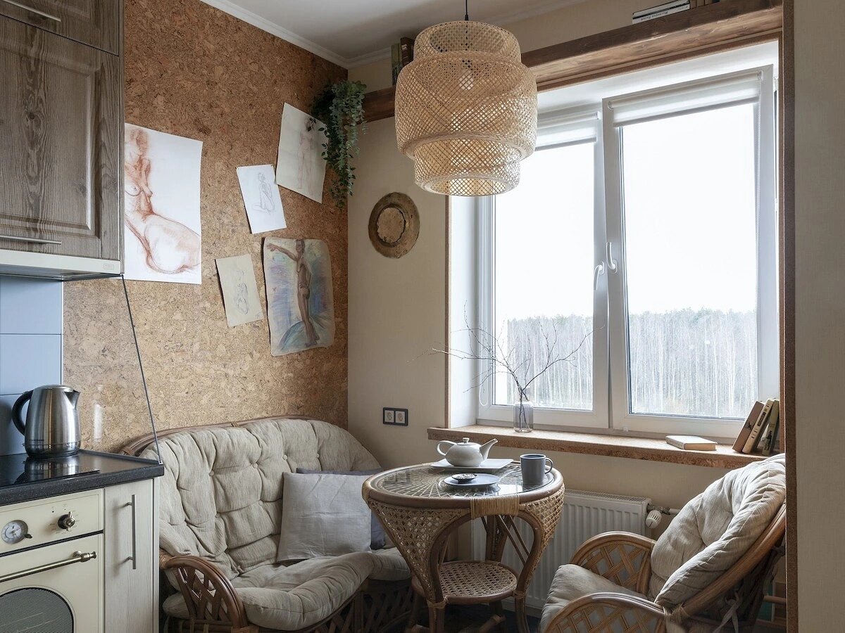 Ближе к окну находится зона отдыха. В её оформлении задействовали натуральные материалы — пробку на стенах, мебель из ротанга, деревянные подоконник и полку. Ротанговые вставки на столике перекликаются с люстрой на потолке.
