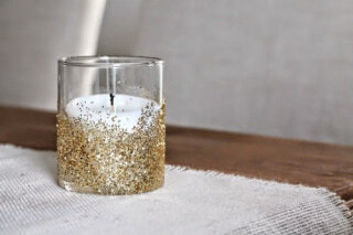 Вам понадобится обычный стакан любого размера и формы, блестки и клей. Нижнюю часть стакана обработайте обработайте клеем и посыпьте большим количеством блесток, дайте высохнуть и поместите на дно стакана свечку. 