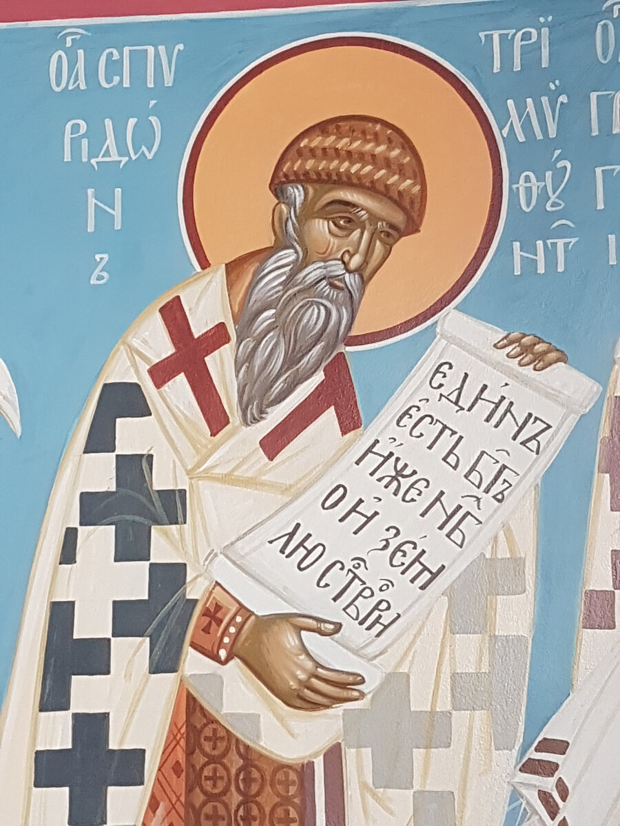 Фрагмент росписи в алтаре придела святителя Николая Мирликийского храма Успения Пресвятой Богородицы "за верхом" г. Калуга.  Спиридон был сыном простых людей, с детства был кроток и скромен, избегал праздных забав, приучен к труду. Вместе с отцом возделывал поле, пас овец. Поэтому святителя Спиридона часто изображают на иконах в пастушьей шапке, сплетенной из ивовых прутьев. Святой в святительском облачении, в руках – либо Евангелие, либо свиток.