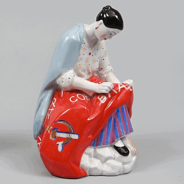 Скульптура "Работница, вышивающая красное знамя".  Выпуск 1967 г. Фарфор. рельеф, лепнина, роспись надглазурная полихромная, позолота. Размер: 14,5 х 9,3 см. Санкт-Петербургское государственное бюджетное учреждение культуры "Государственный музей истории Санкт-Петербурга". https://goskatalog.ru/