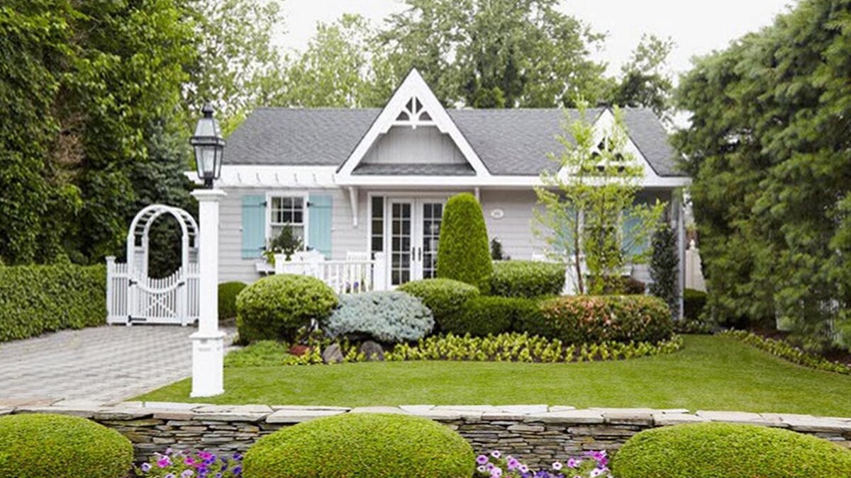 Уютный и очень скромный одноэтажный домик, как у доброй феи. Светлые стены, изящный ажур деревянного декора и мелкое членение оконных переплётов – излюбленные мотивы «женской» архитектуры. Оградка и фонарь дополнили гарнитур. МИ-МИ-МИ